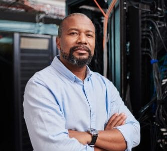 Experienced engineer standing with arms crossed in a server room