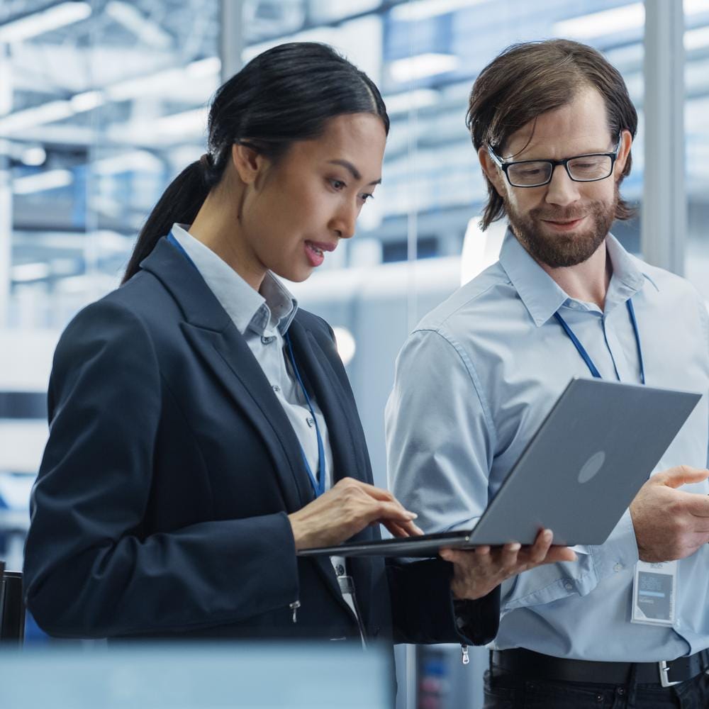 Two industrial engineers reviewing a laptop in a technology factory