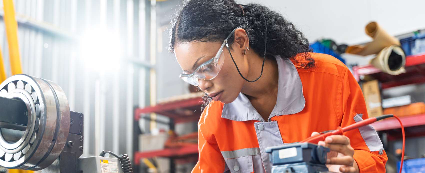 Technician in safety glasses testing an electric motor with a multimeter in a repair workshop