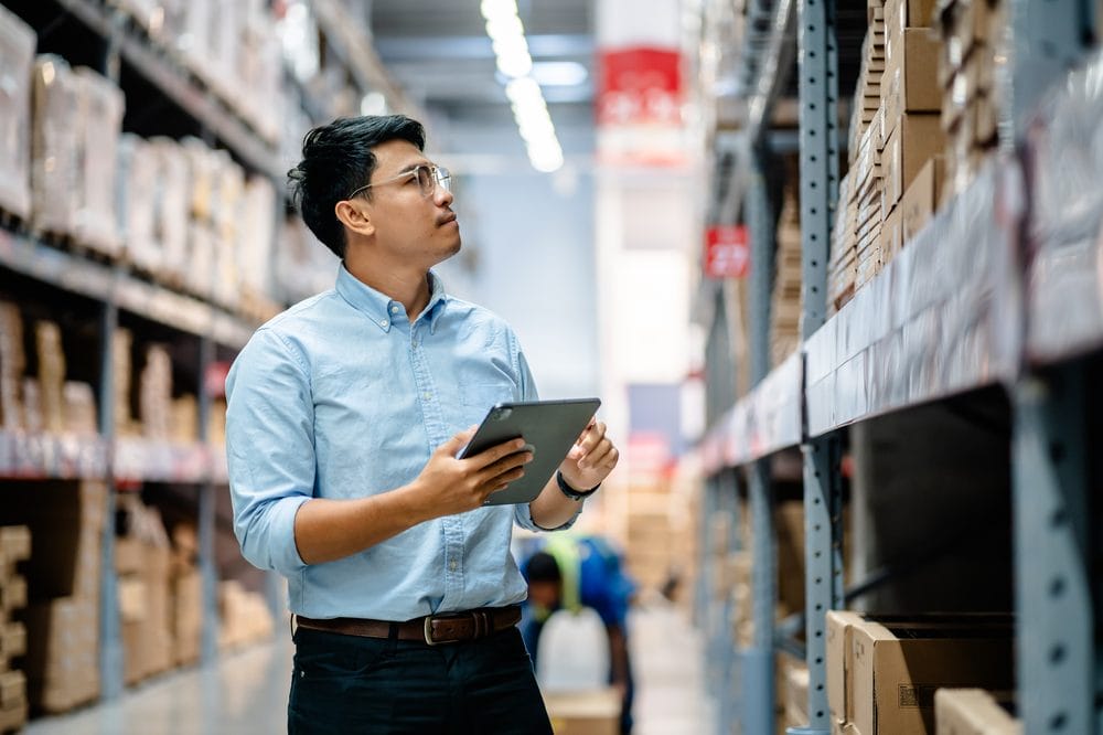 Manager checking stock inventory on warehouse shelves with a tablet