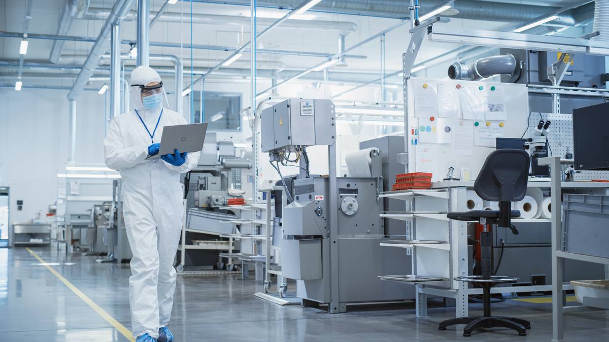 Technician in sterile coverall reviewing machine settings on a clean production floor