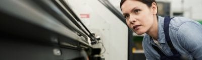Factory technician in workwear watching a lathe machine and adjusting it during processing