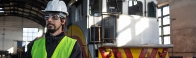 Engineer with a tablet beside a locomotive in a train repair shop